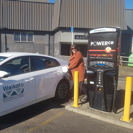 An image of a lady plugging a charger into an electric vehicle