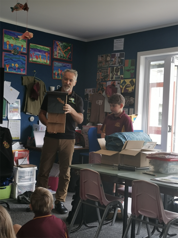 Image of a man holding up a wooden bat hotel in front of a group of students