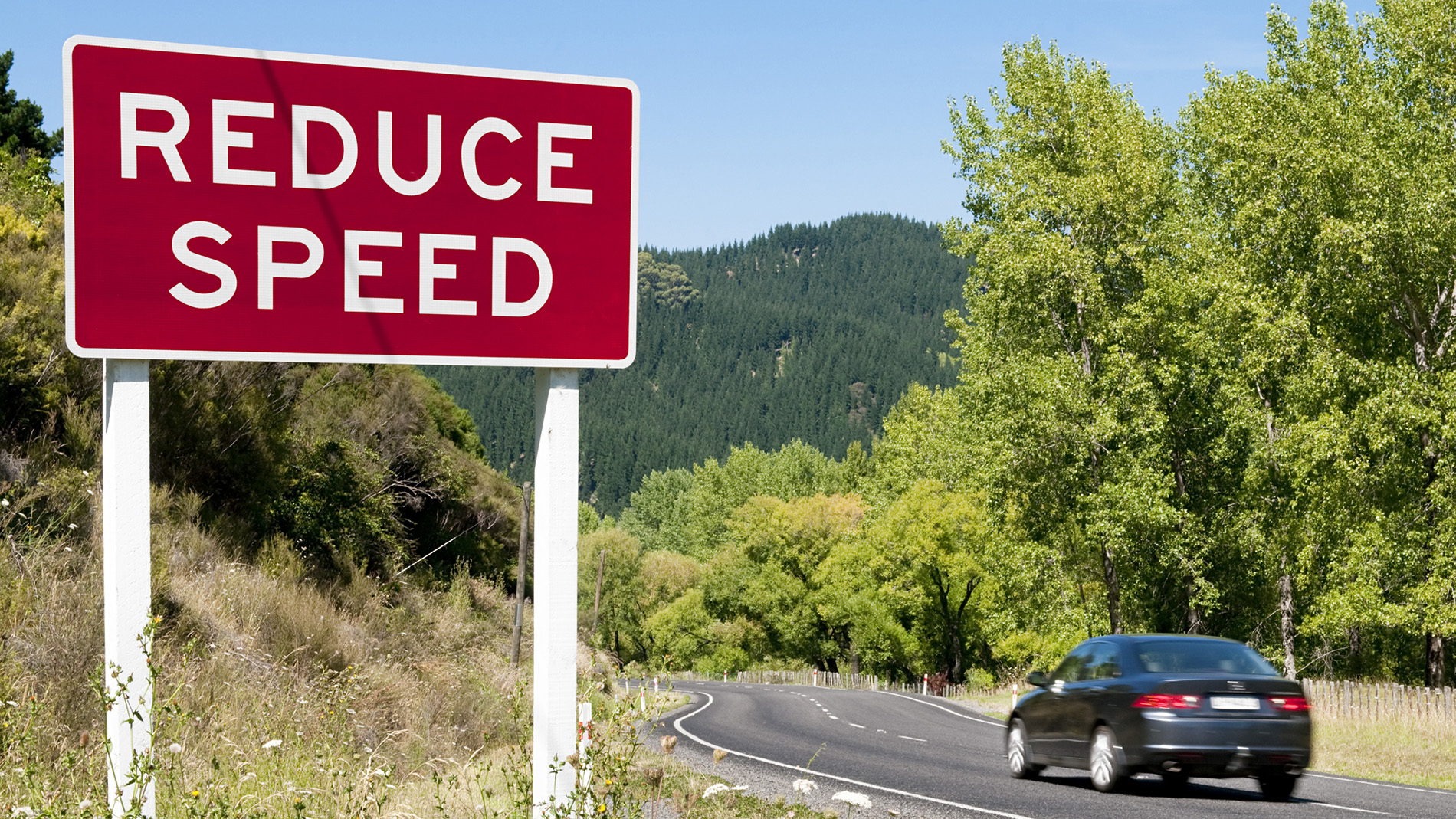 Car on winding road with reduce speed sign on roadside 