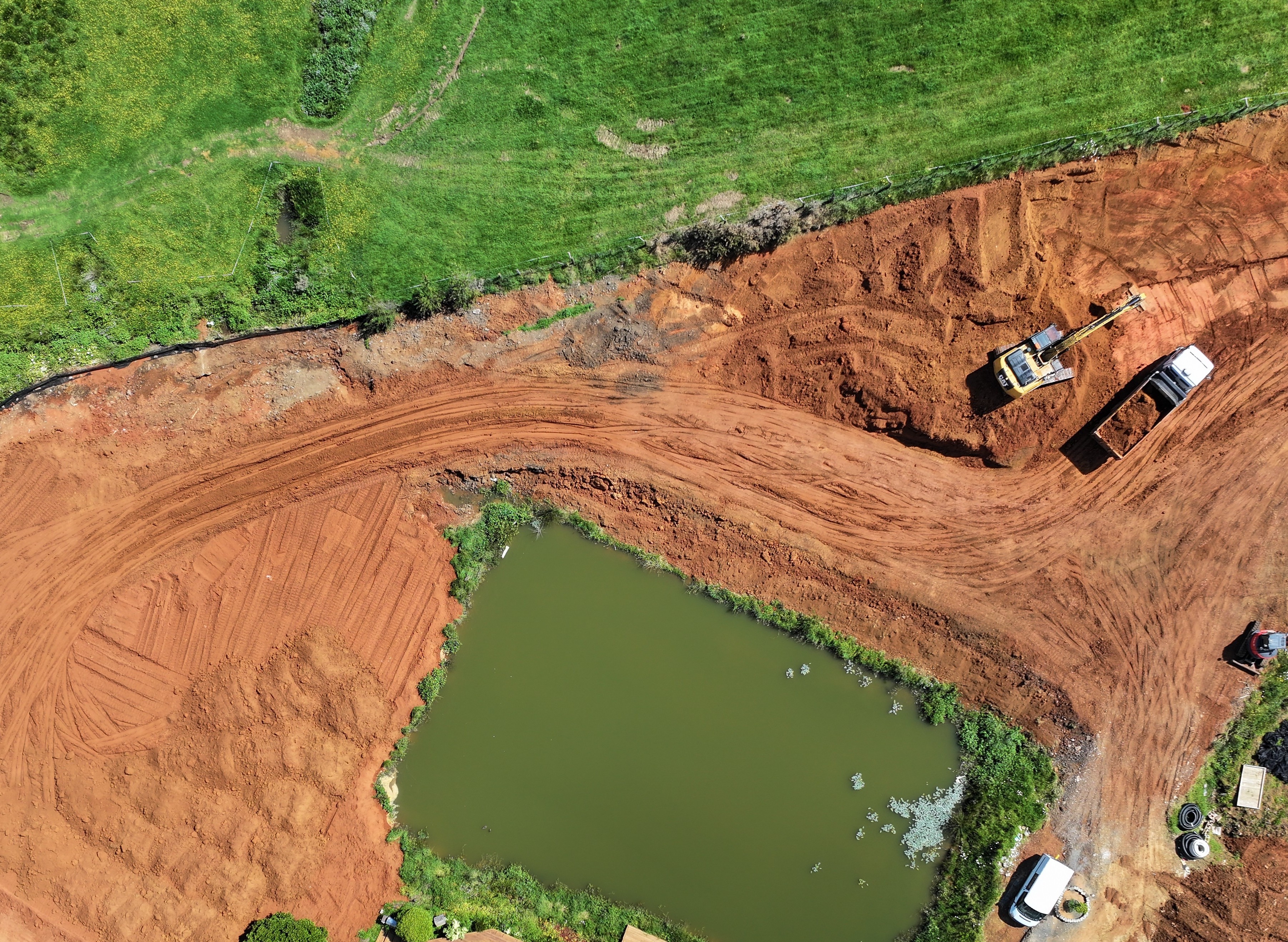 Aerial drone view of an excavated site with machinery beside a green water-filled pond