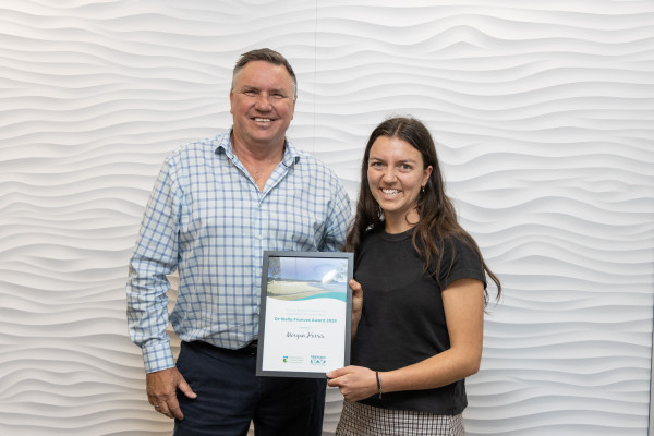Man and woman standing side by side smiling. Woman is holding a framed certificate.